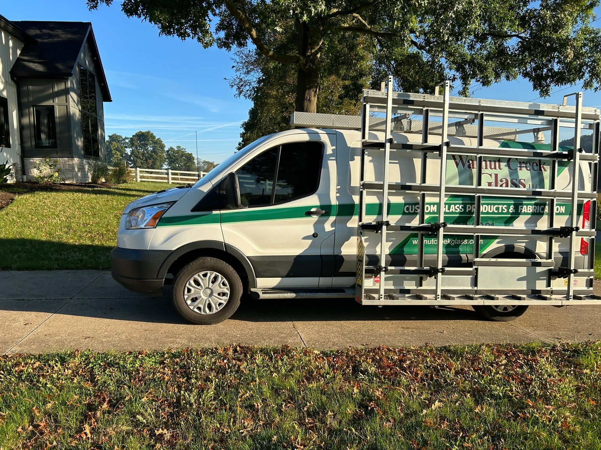 A white van with a ladder on the back is parked on the side of the road.