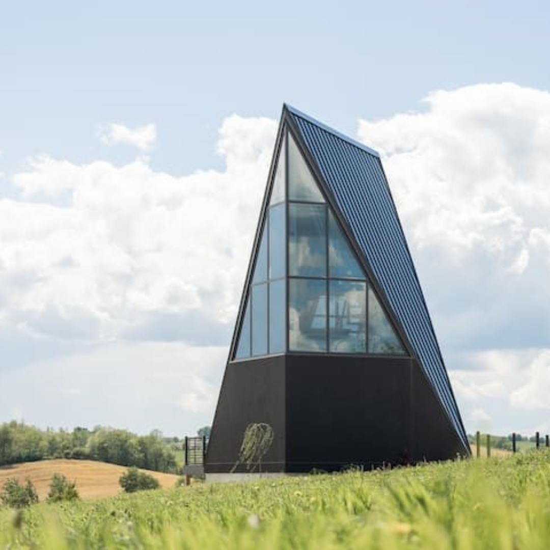 A black building with a triangle shaped roof is sitting on top of a grassy hill.