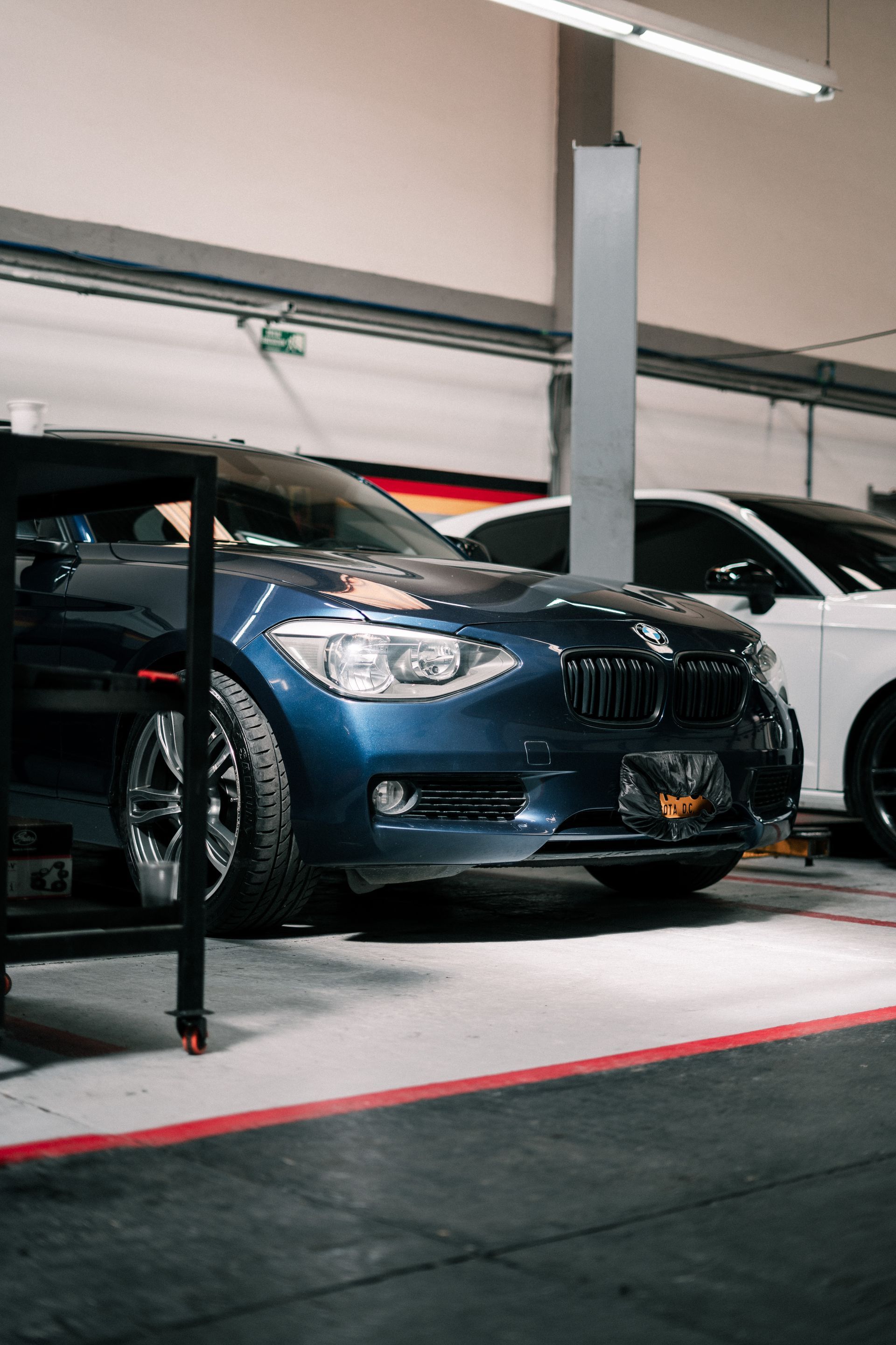 A blue car is parked in a garage next to a white car.