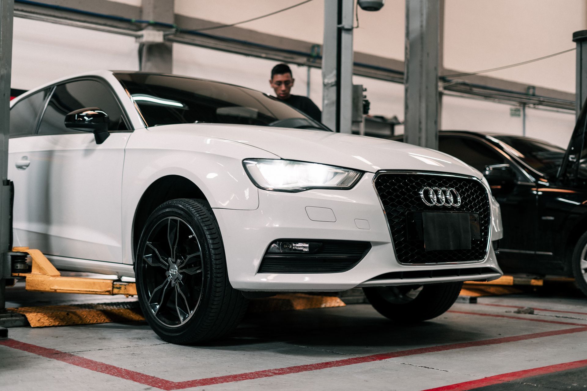 A white audi a3 is sitting on a lift in a garage.