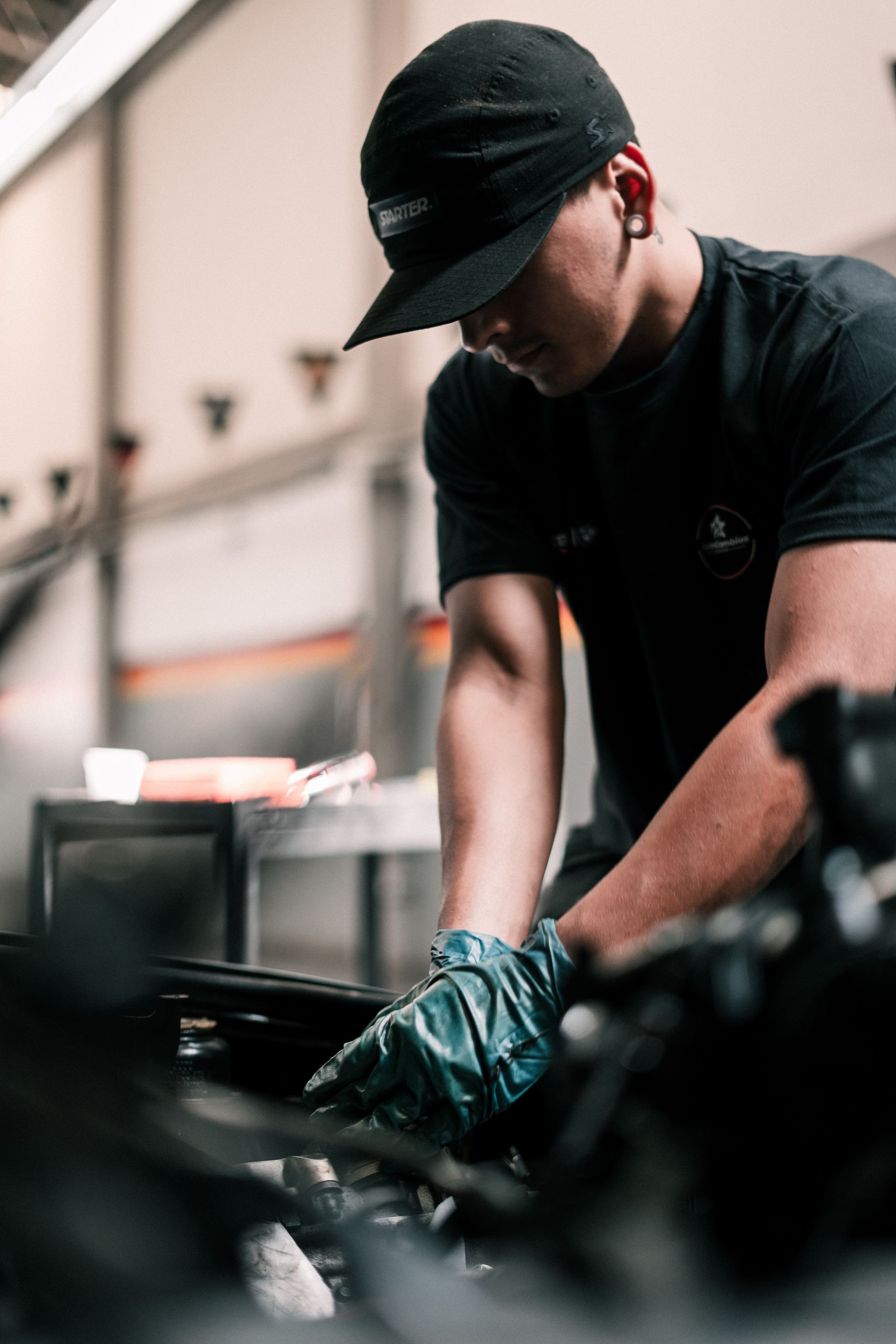 A man wearing a hat and gloves is working on a car engine.