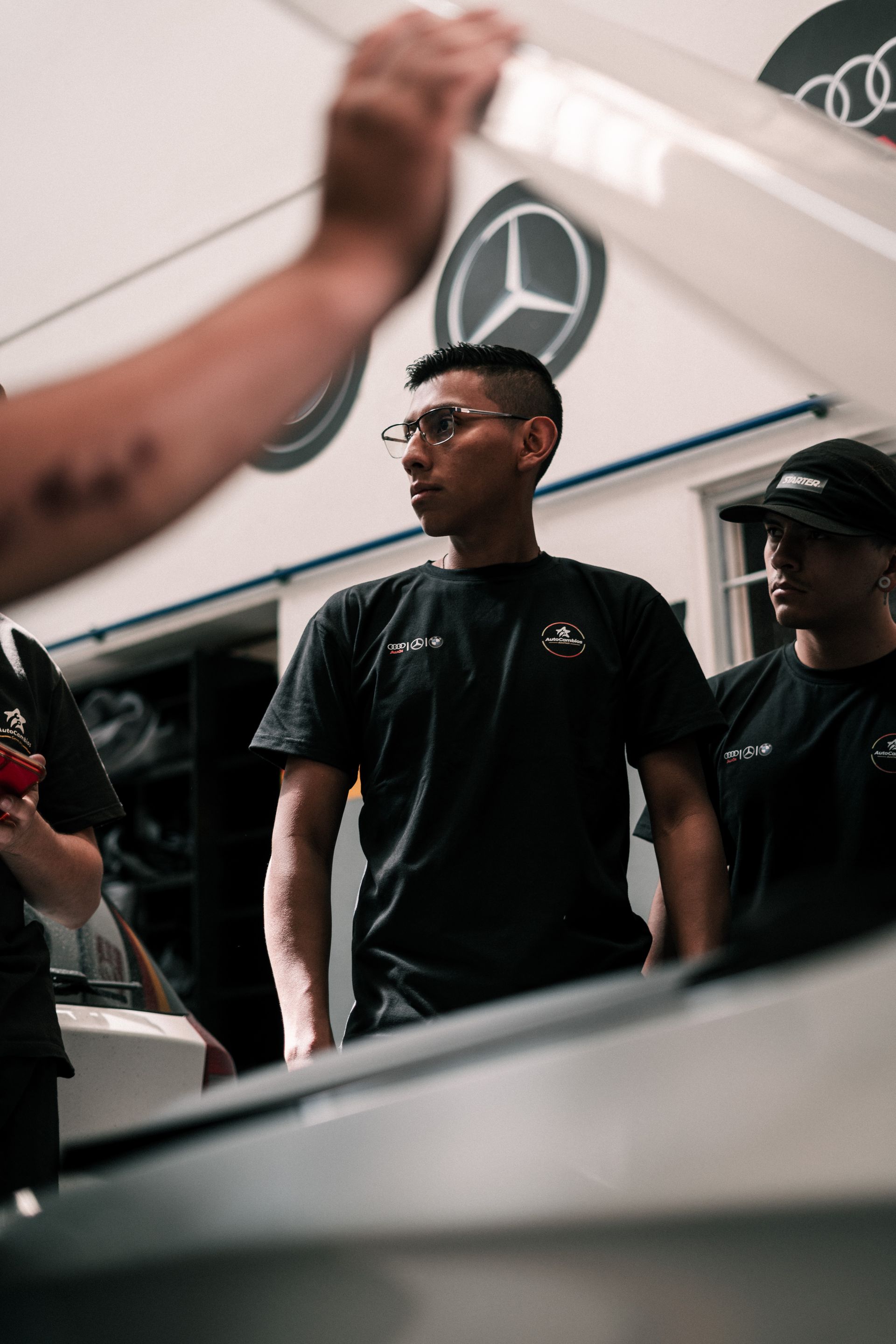 A group of men are standing in front of a car in a garage.