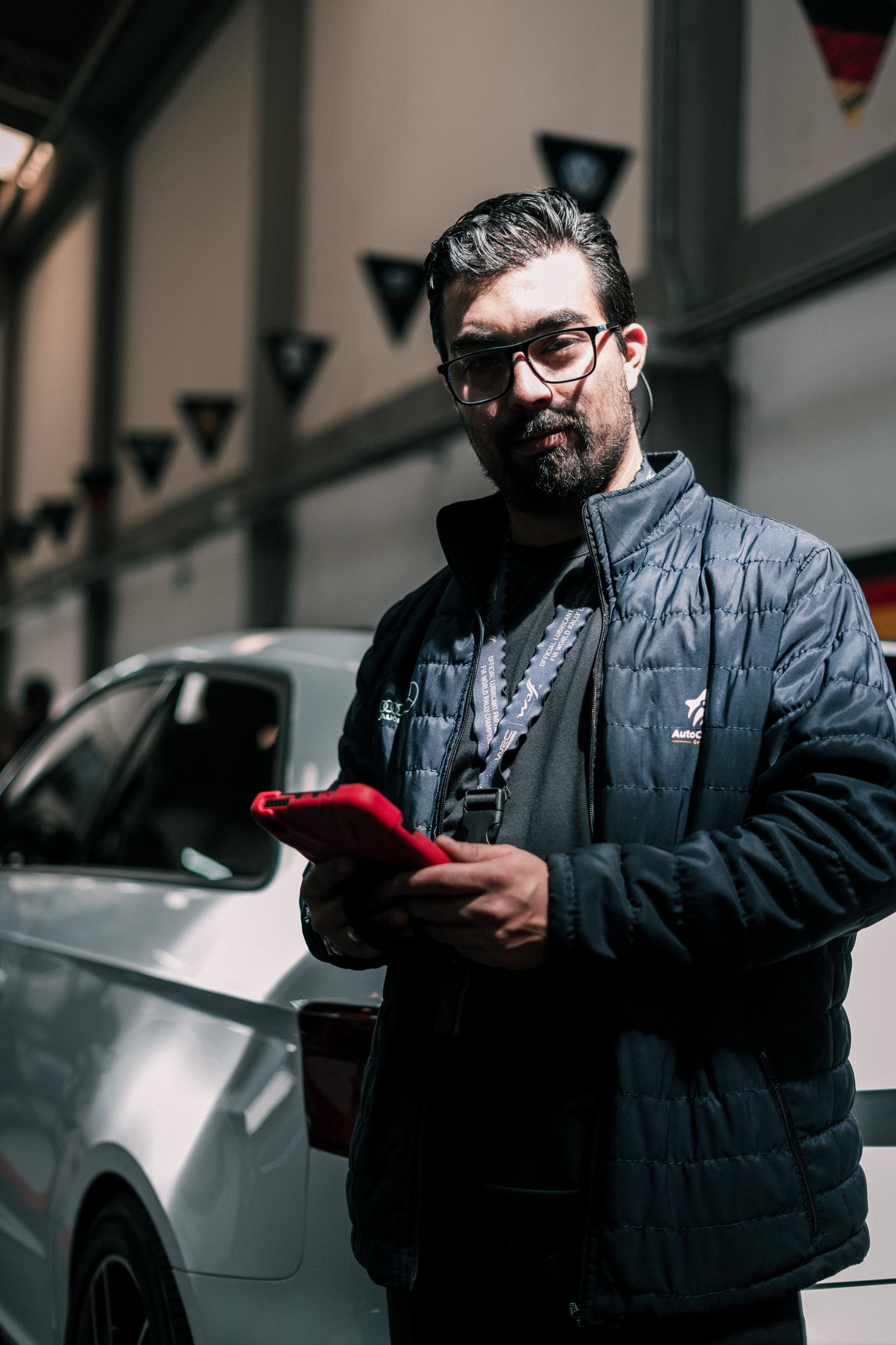 A man in a black jacket is standing in front of a white car.
