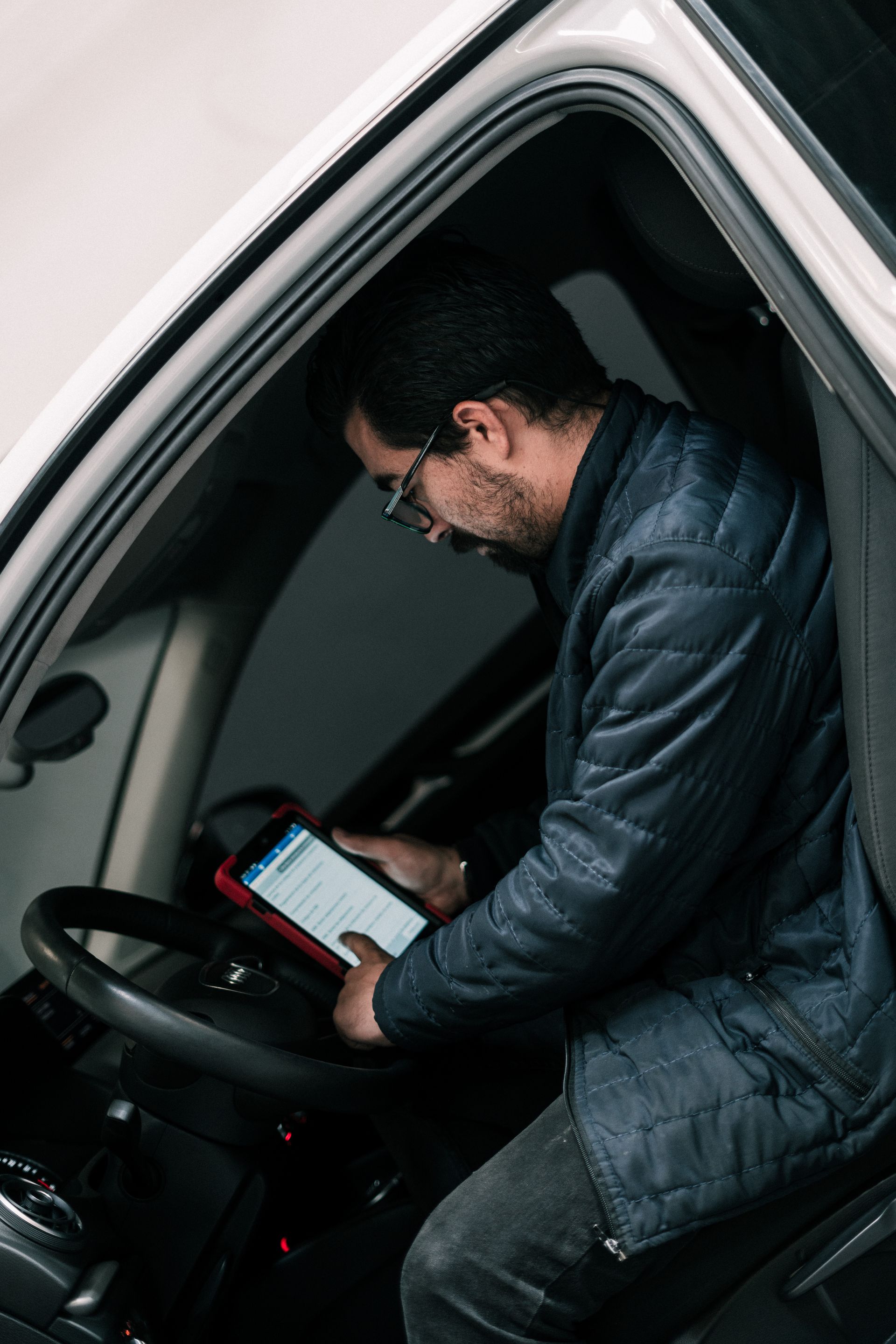 A man is sitting in a car looking at a tablet.