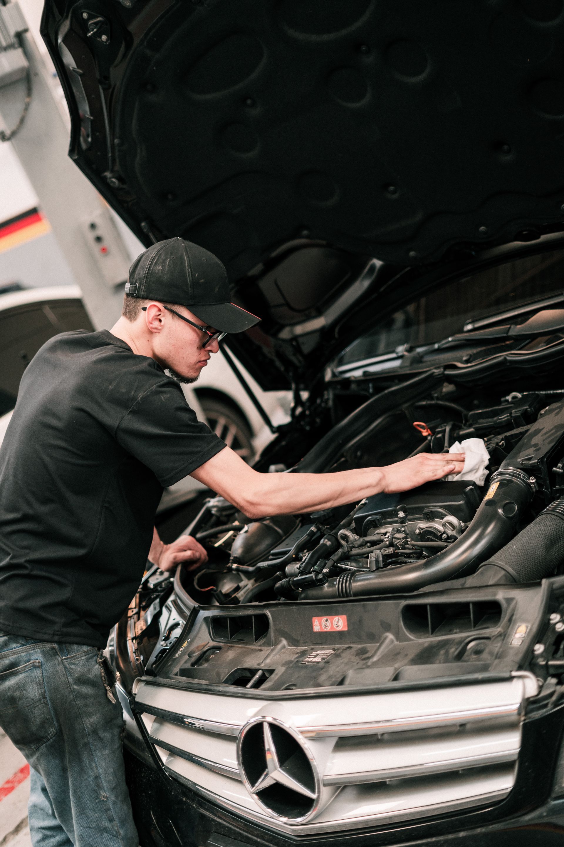 A man is working on the engine of a mercedes with the hood open.