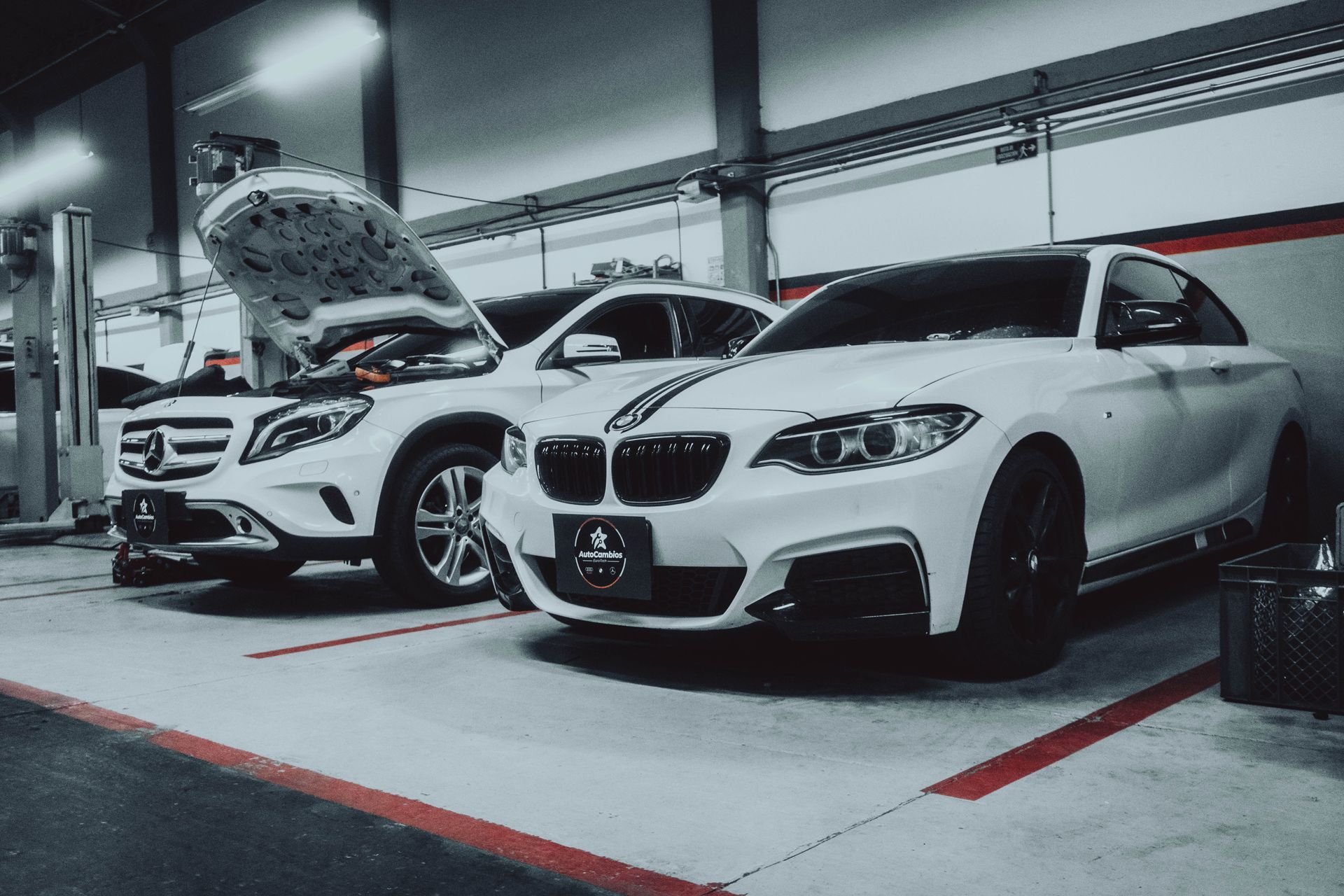 Two white cars are parked next to each other in a garage.