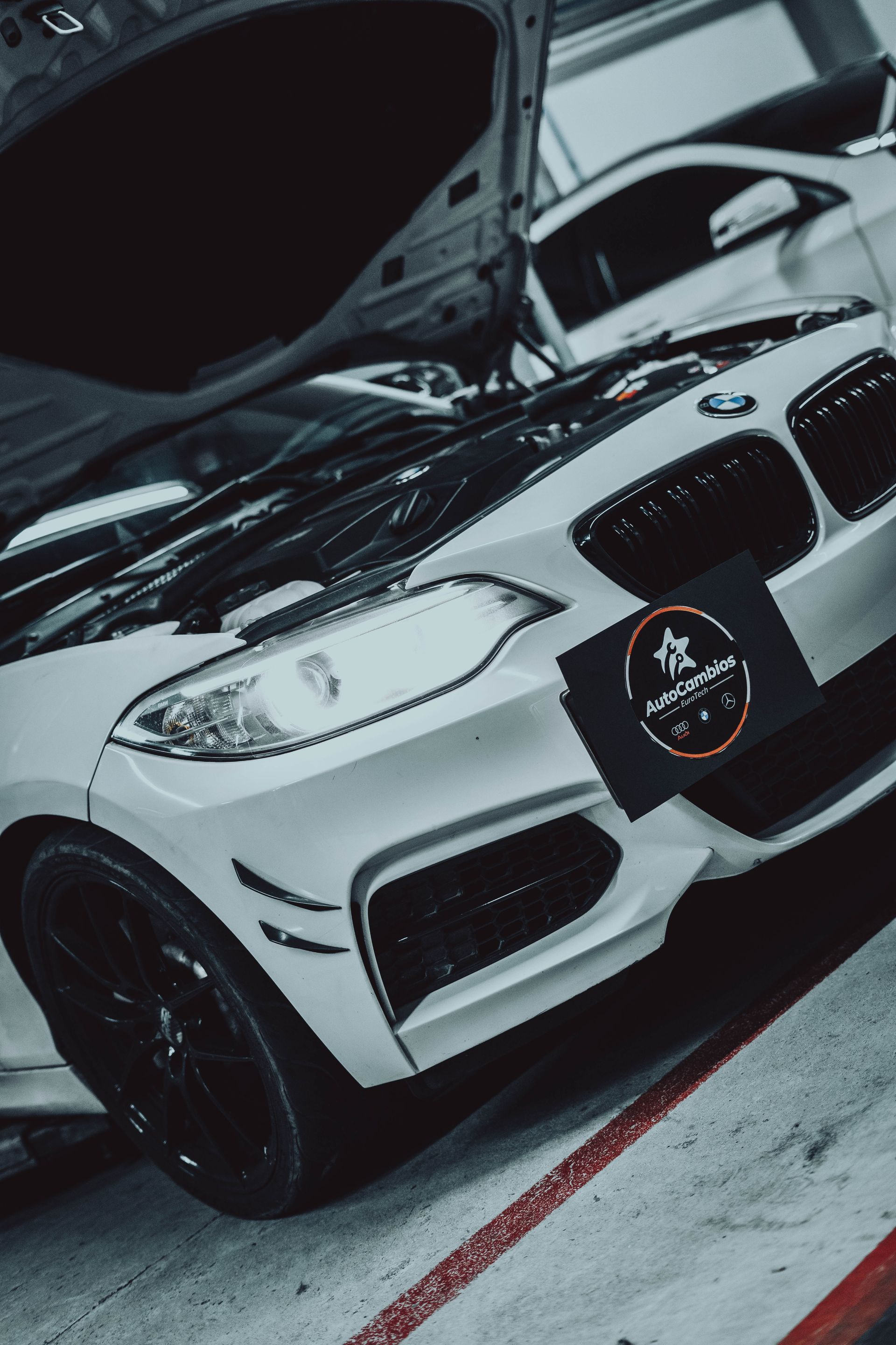 A white bmw with the hood open is parked in a garage