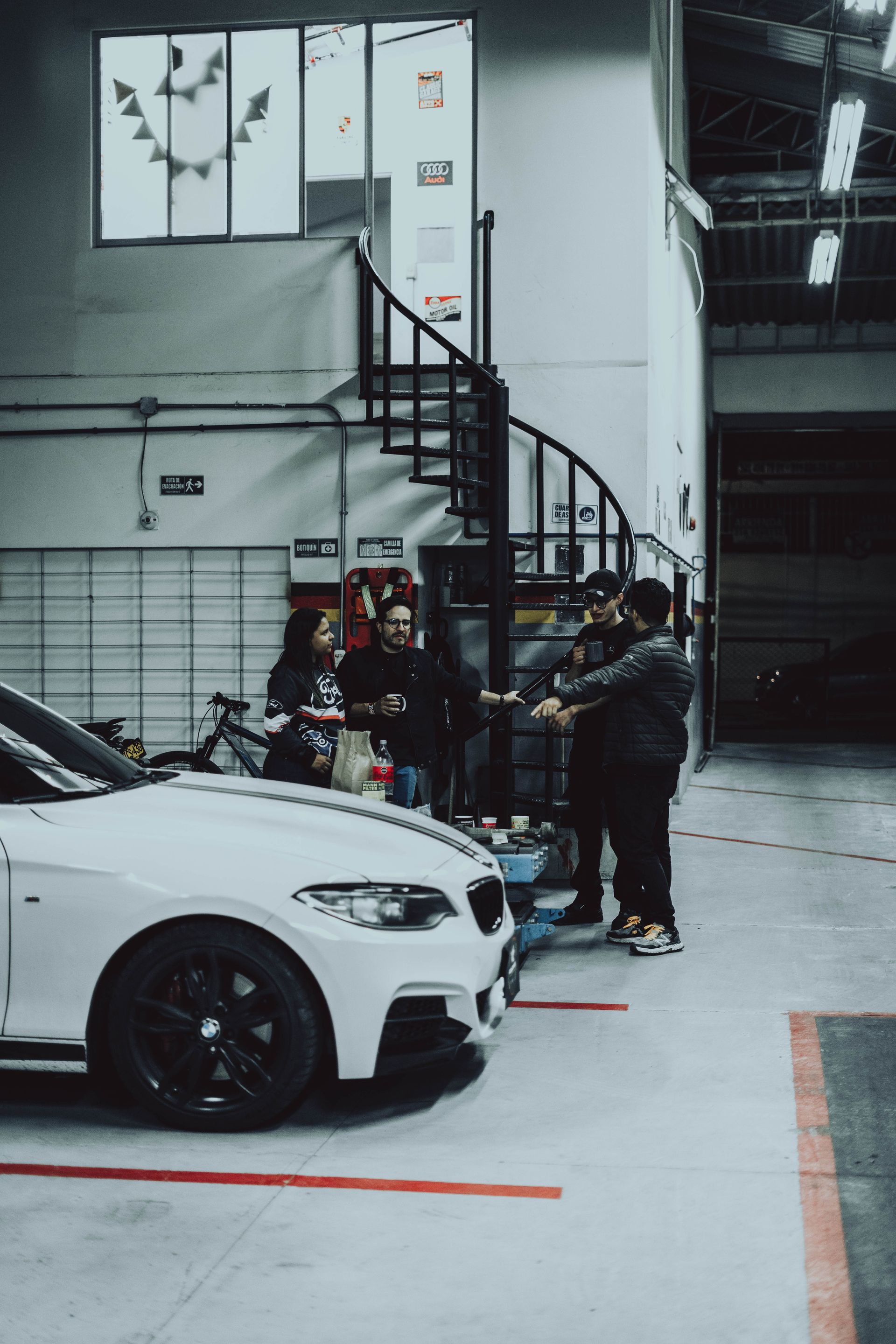 A group of people are standing around a white car in a garage.