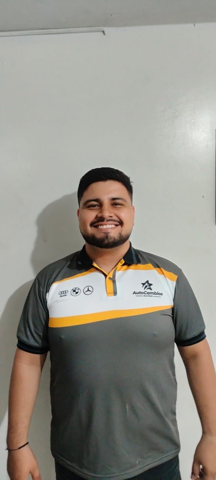 A man with a beard is wearing a gray and yellow polo shirt.