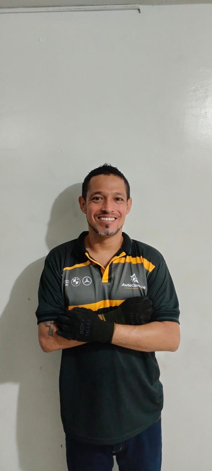 A man is standing with his arms crossed in front of a white wall.