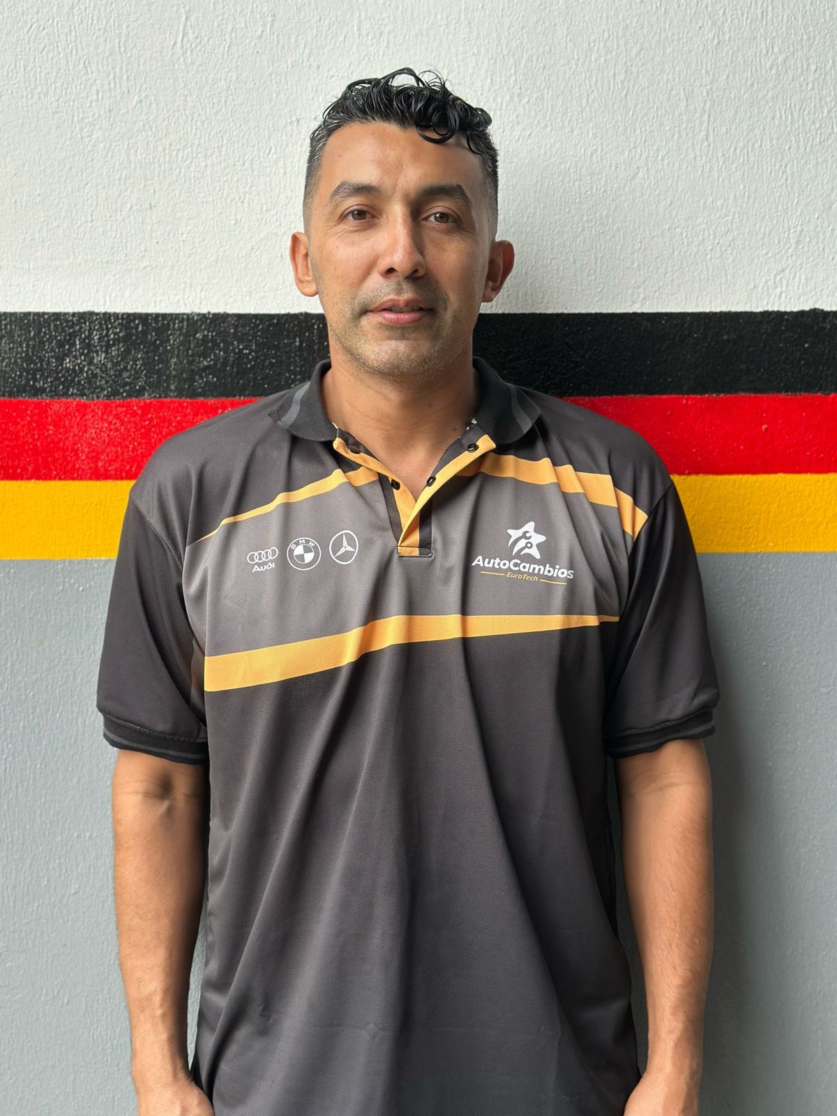 A man in a black and gold shirt stands in front of a german flag