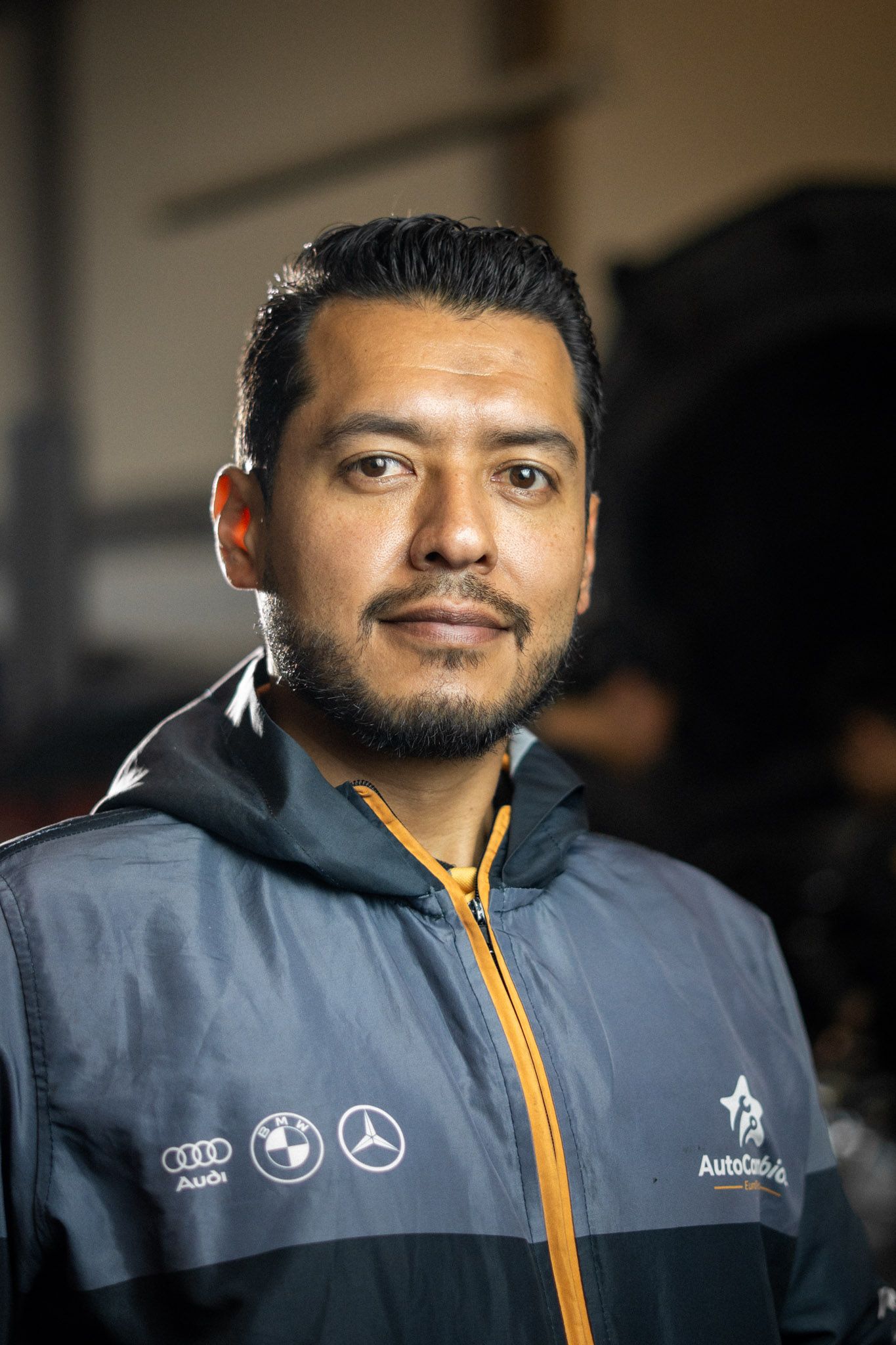 A man with a beard is wearing a jacket with logos on it.