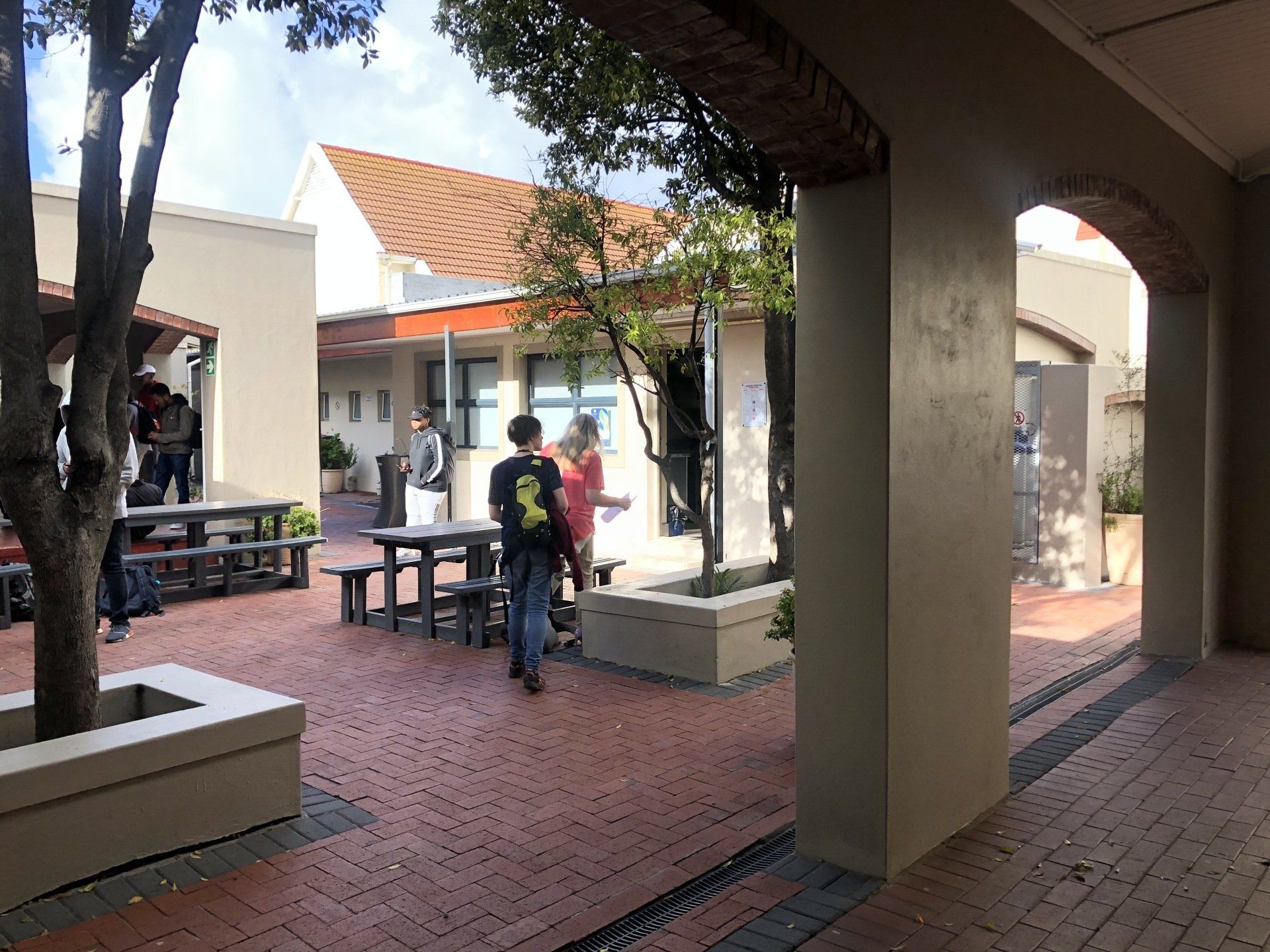 a group of students are walking through a courtyard with tables and benches .