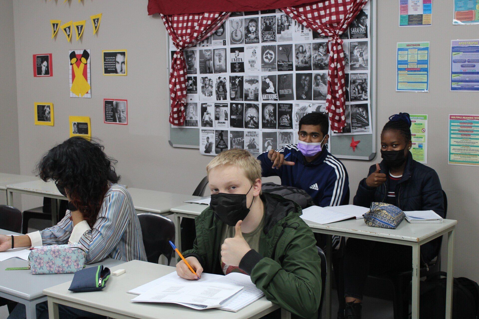 a group of students wearing face masks are sitting at desks in a classroom .