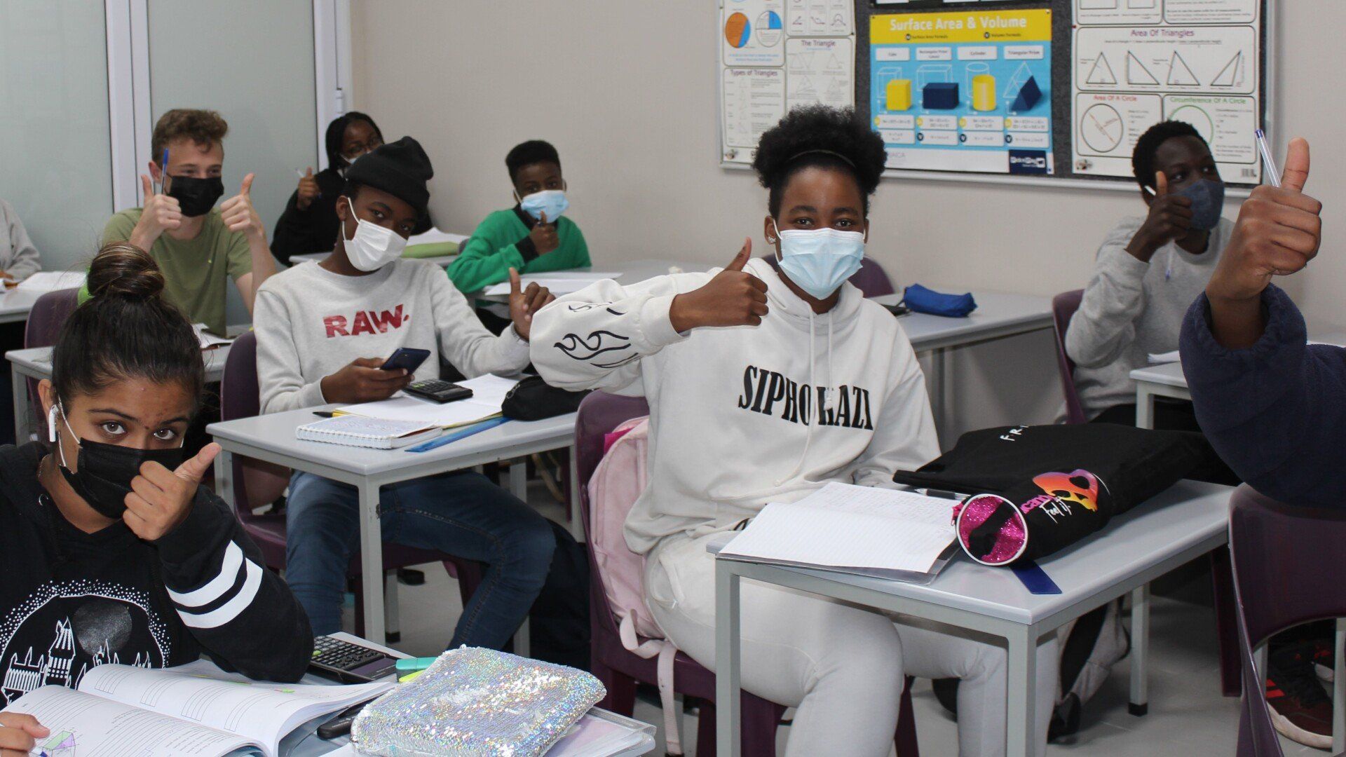 a group of students wearing face masks are sitting at desks in a classroom .