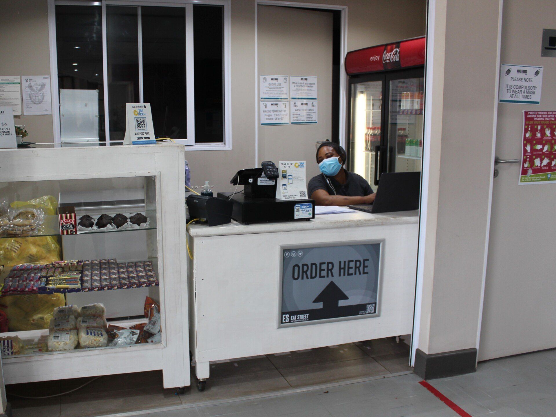 a woman wearing a mask is behind a counter that says order here