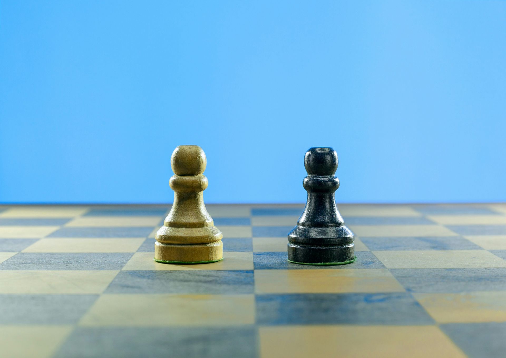White and black chess pawns face each other on a chessboard against a blue background.