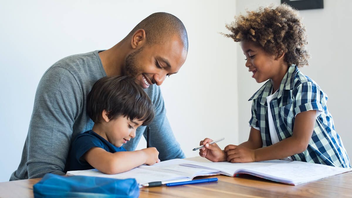 A man is helping two young boys with their homework at a table.
