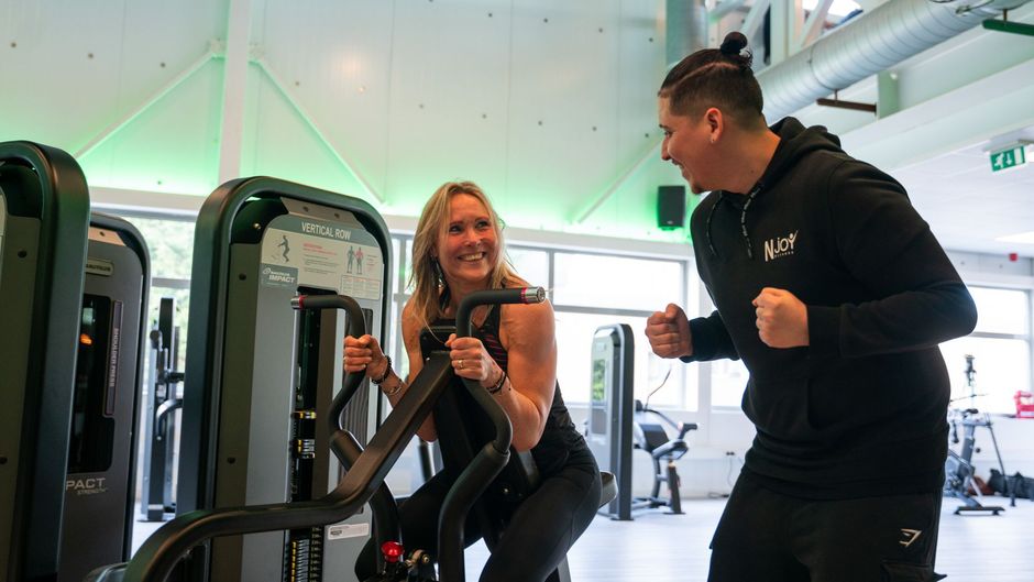 Een man en een vrouw fietsen op een hometrainer in een sportschool.