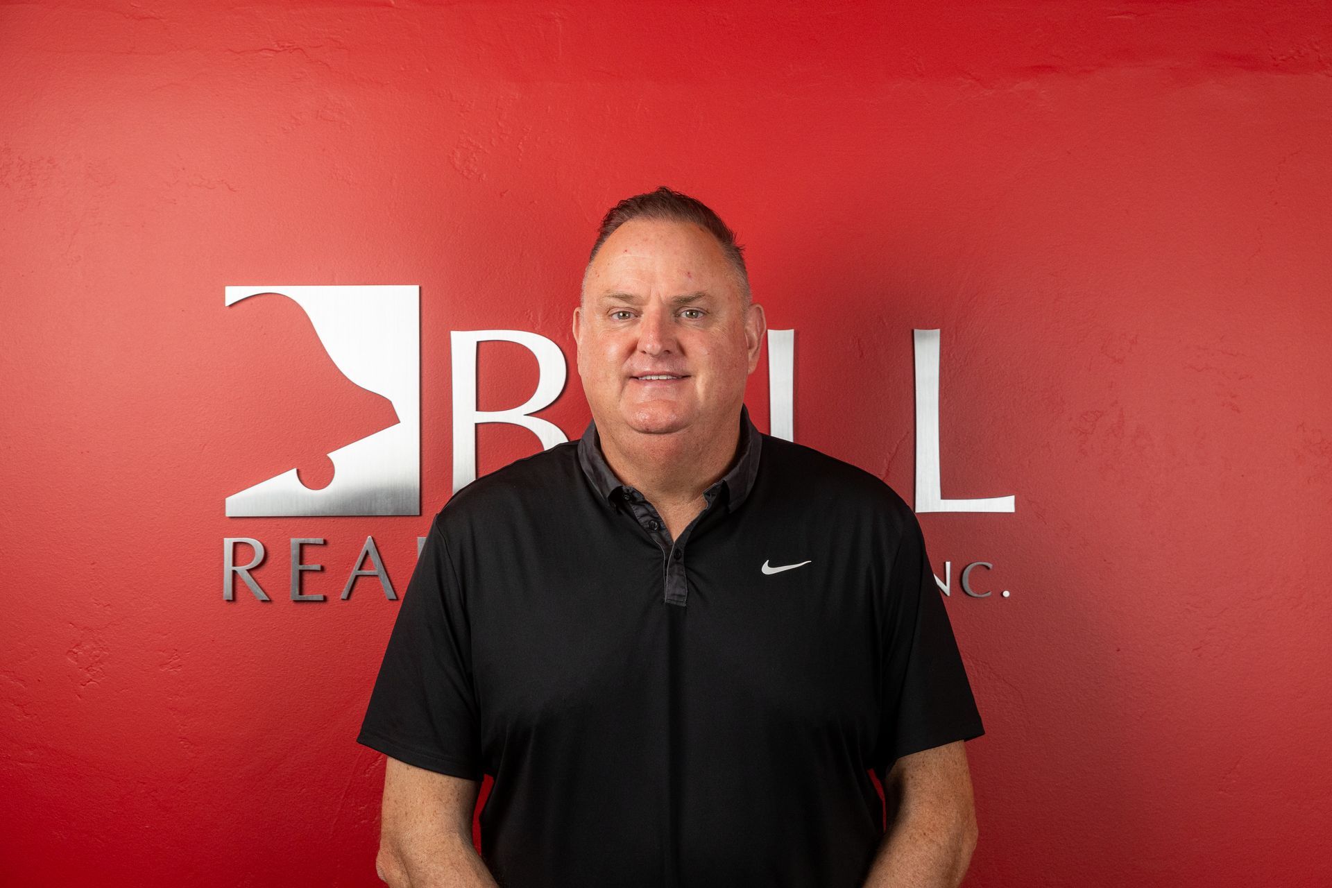 A man in a black shirt is standing in front of a red wall.