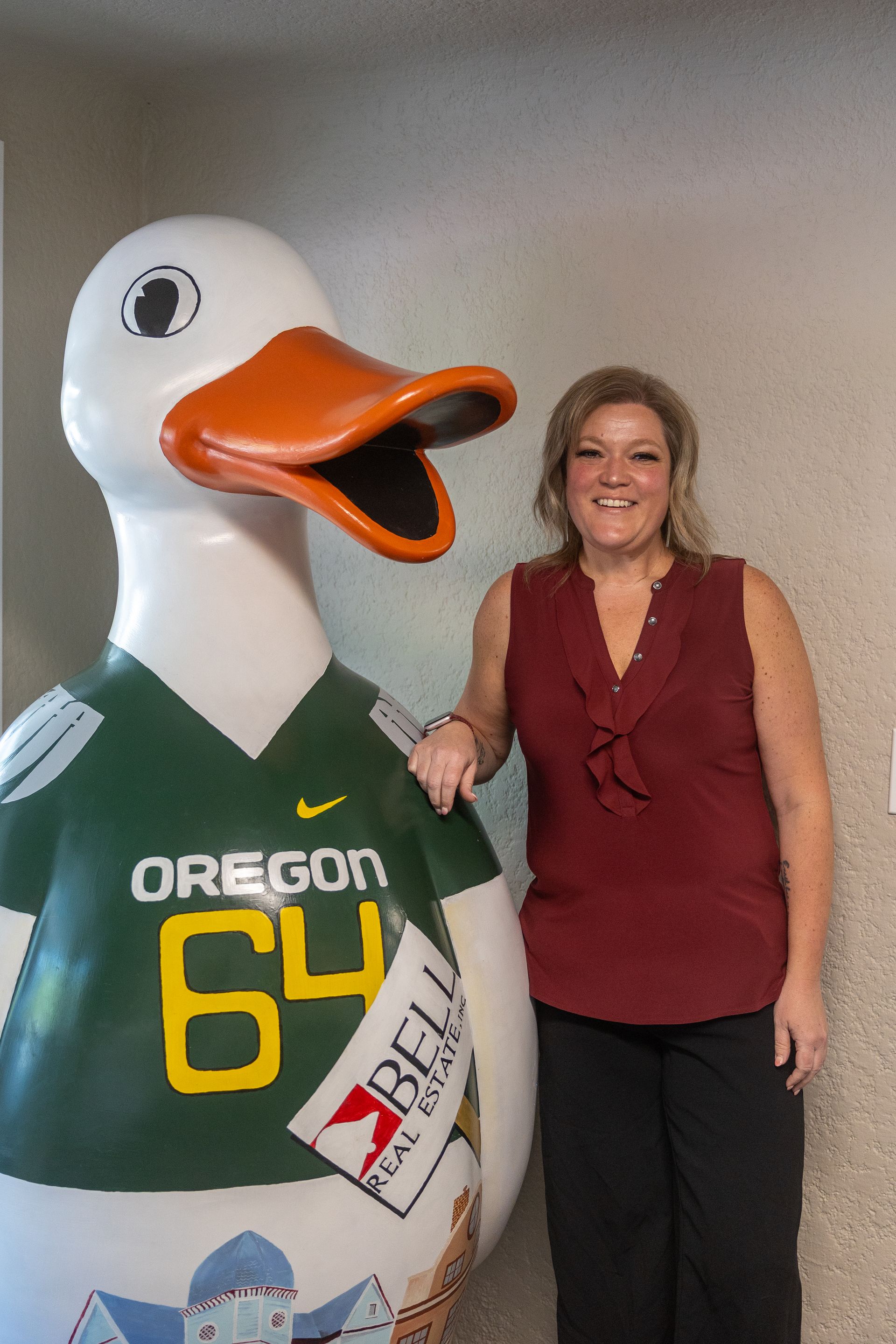 A woman is standing next to a statue of a duck wearing an oregon jersey