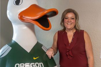 A woman is standing next to a statue of a duck wearing an oregon jersey.
