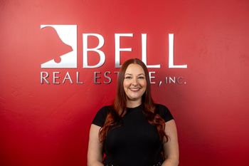 A woman is standing in front of a bell real estate sign.