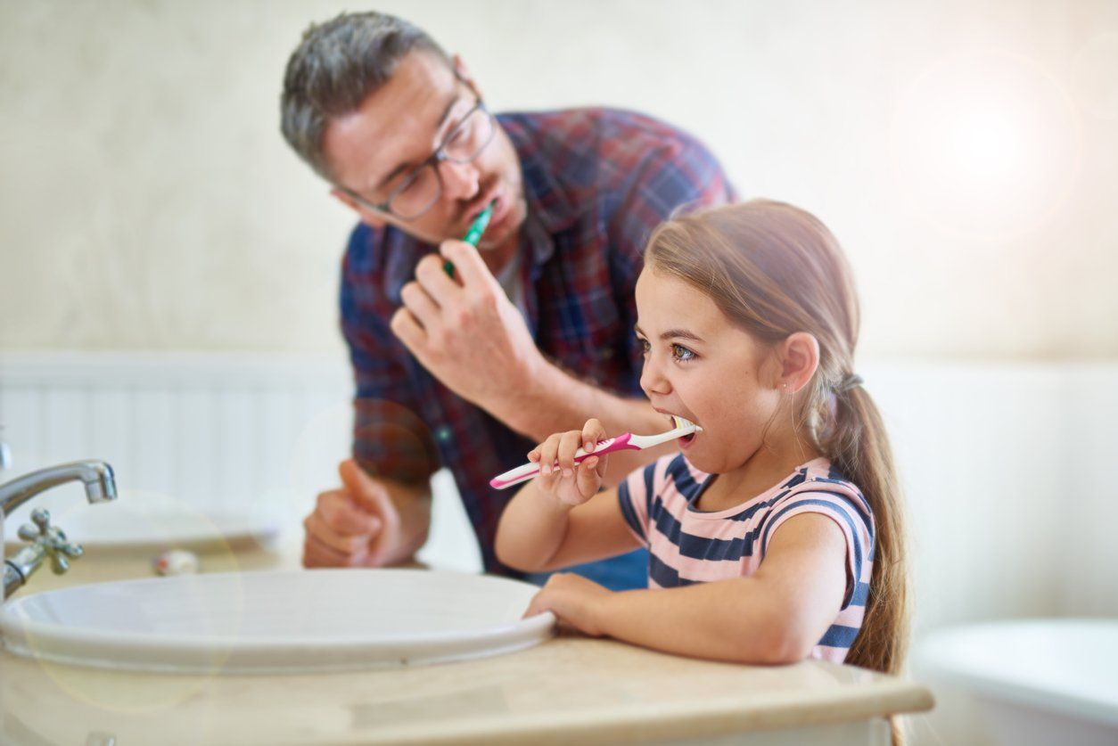 father and daughter preforming good oral hygiene by brushing their teeth