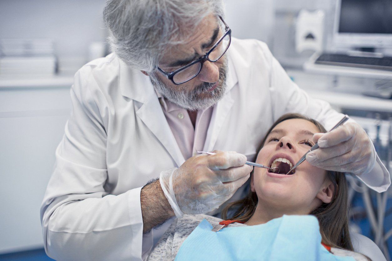 Dentist examining and cleaning a girl's mouth for gum disease.