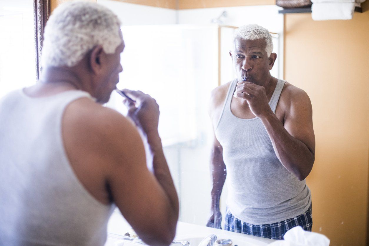 older man brushing his teeth in front of mirror. taking care of teeth as you get older