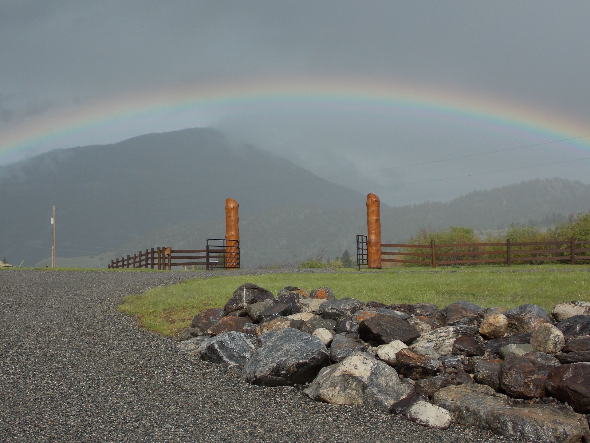 A rainbow is visible over a rock wall and a fence.