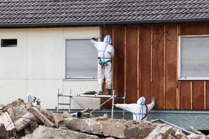 Workers on scaffolding repairing a building’s exterior wall beside piles of rubble