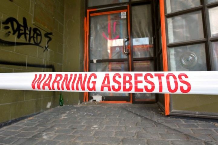 Warning asbestos tape across a building entrance with a window and graffiti in the background