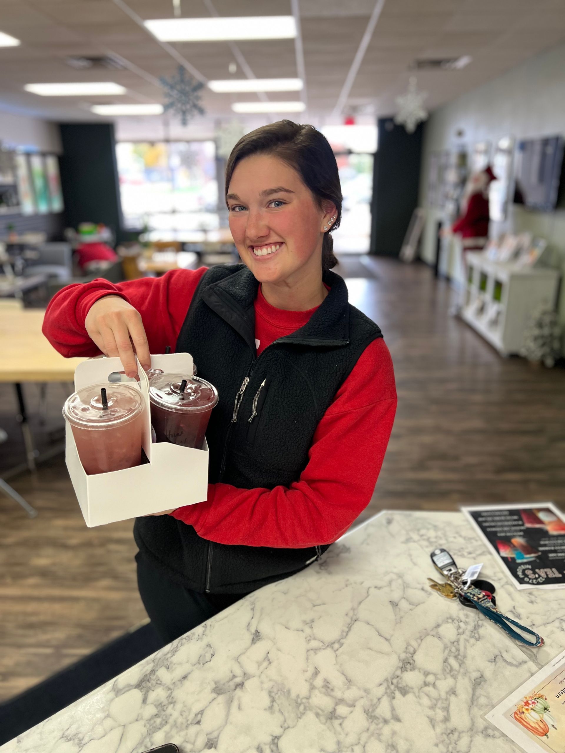 A woman in a red shirt is holding a tray of drinks.