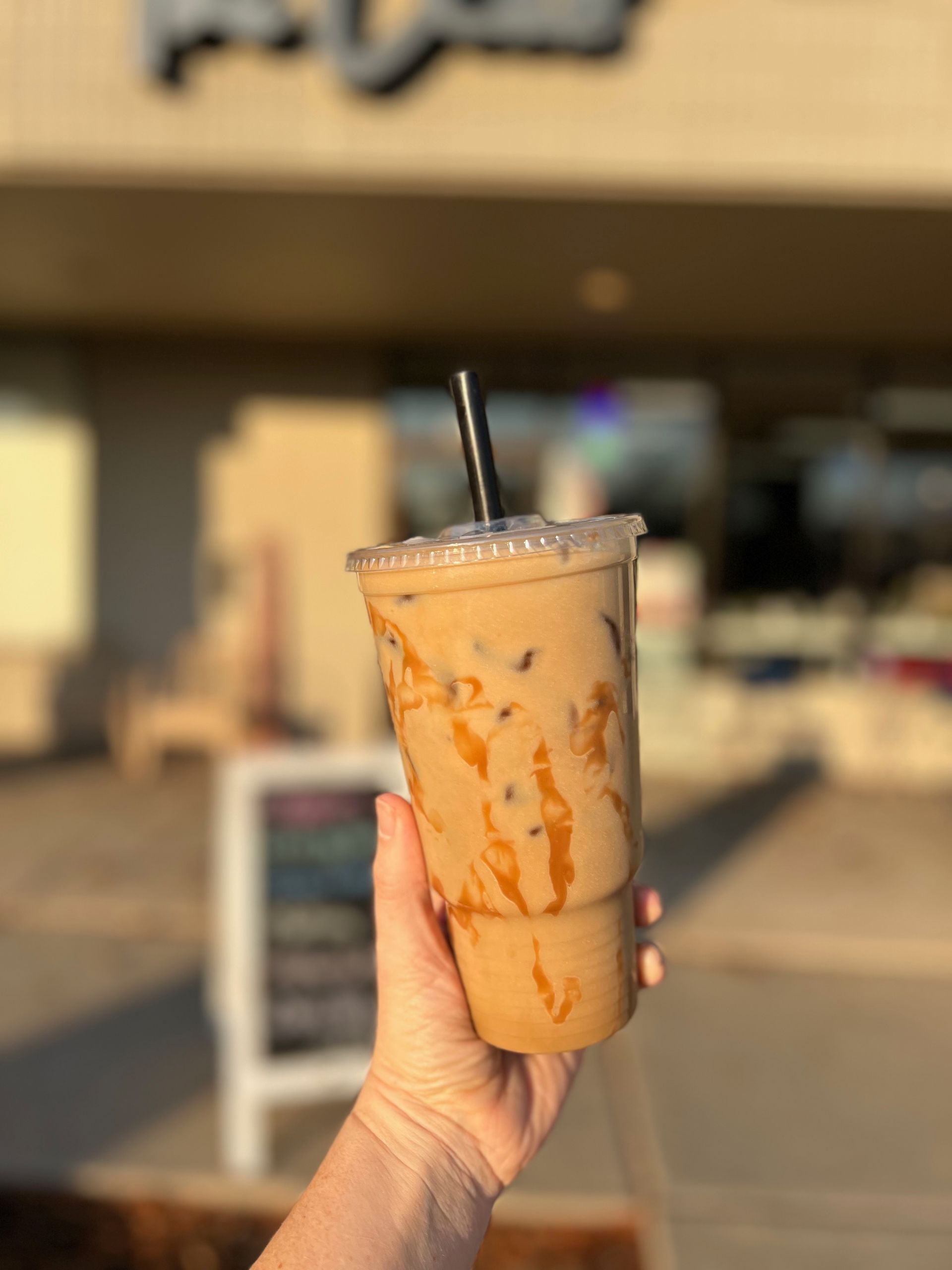 A person is holding a cup of iced coffee with a straw.