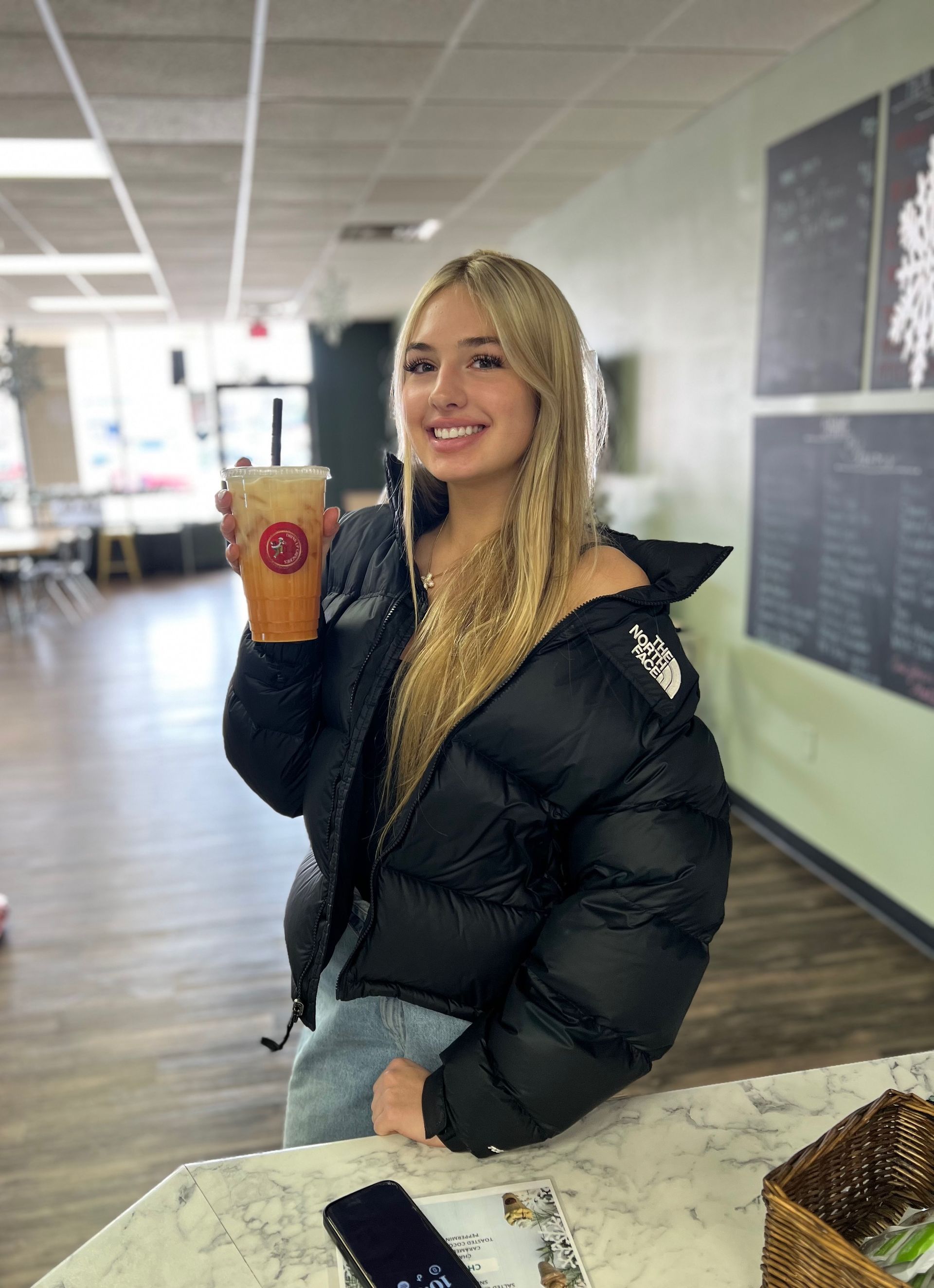 A woman in a black jacket is holding a cup of orange juice.