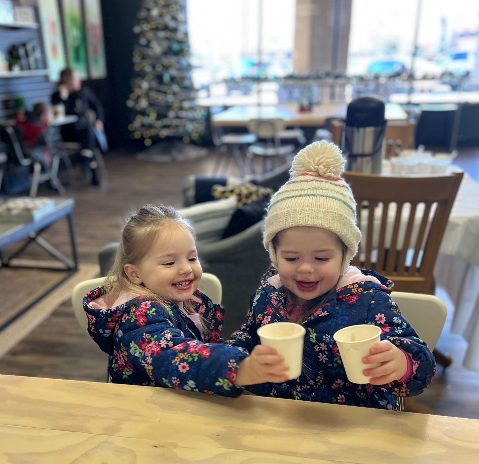 Two little girls are sitting at a table holding cups.