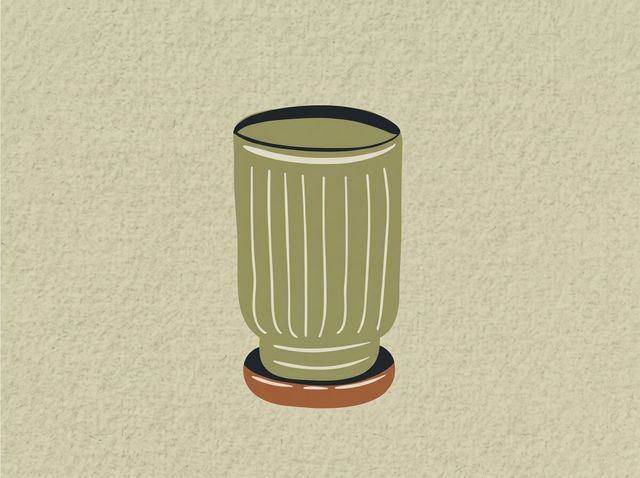 Tall green ribbed vase with a dark rim on a small brown base against a beige wall.