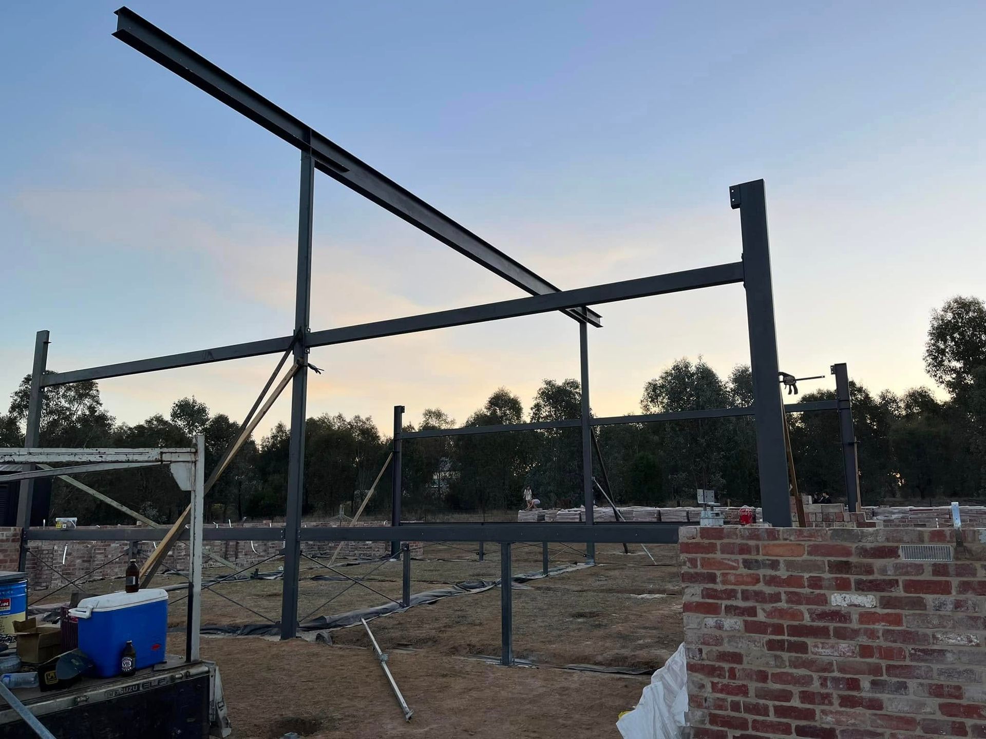 Steel framework of a building under construction, set against a sunset.