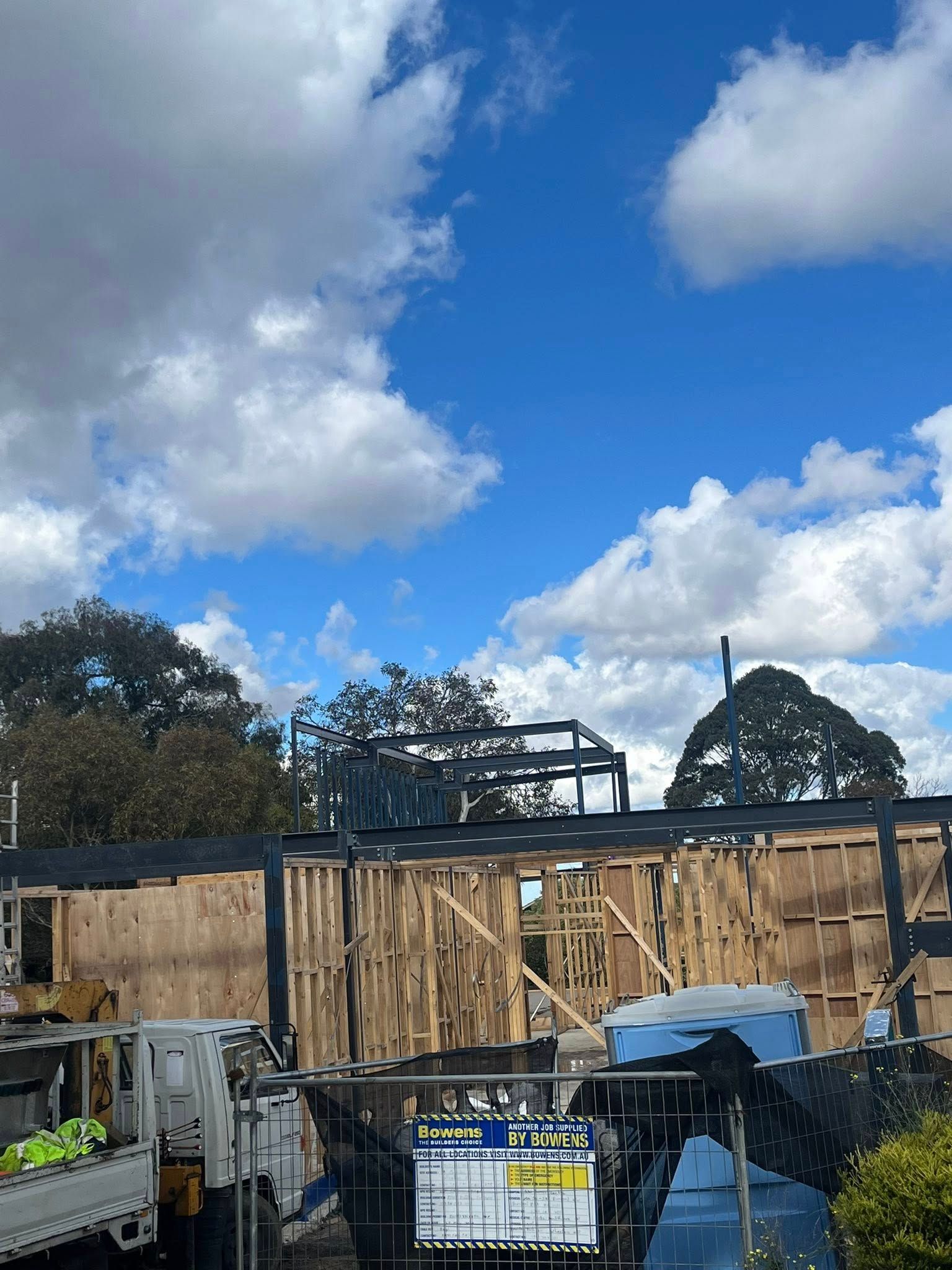 Construction site with exposed wooden framing and charred structure against a blue sky with clouds.