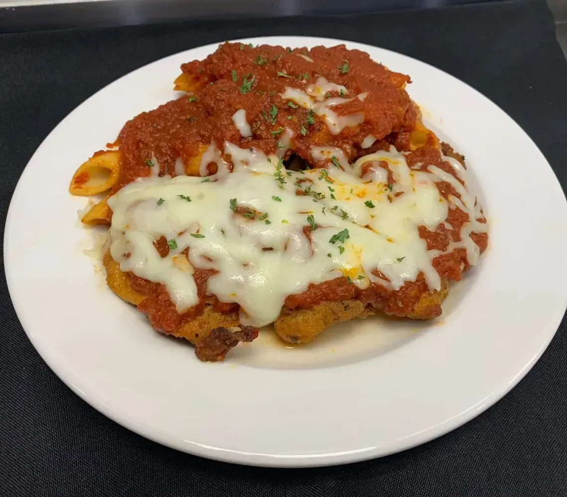 A breaded chicken parmigiana topped with melted mozzarella, marinara sauce, and herbs, served with penne pasta.