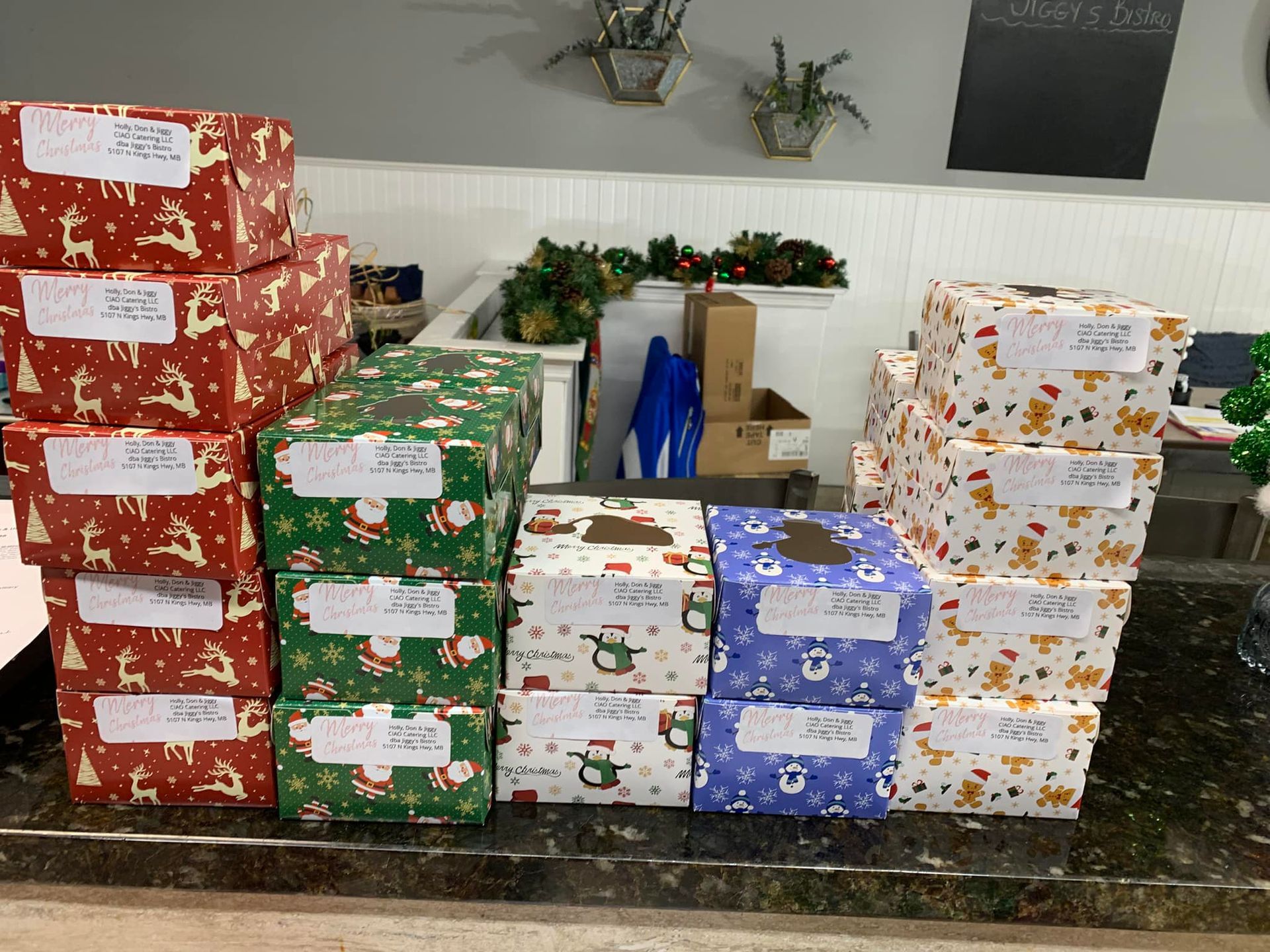 A collection of neatly wrapped Christmas gifts with handwritten address labels sitting on a dark countertop.