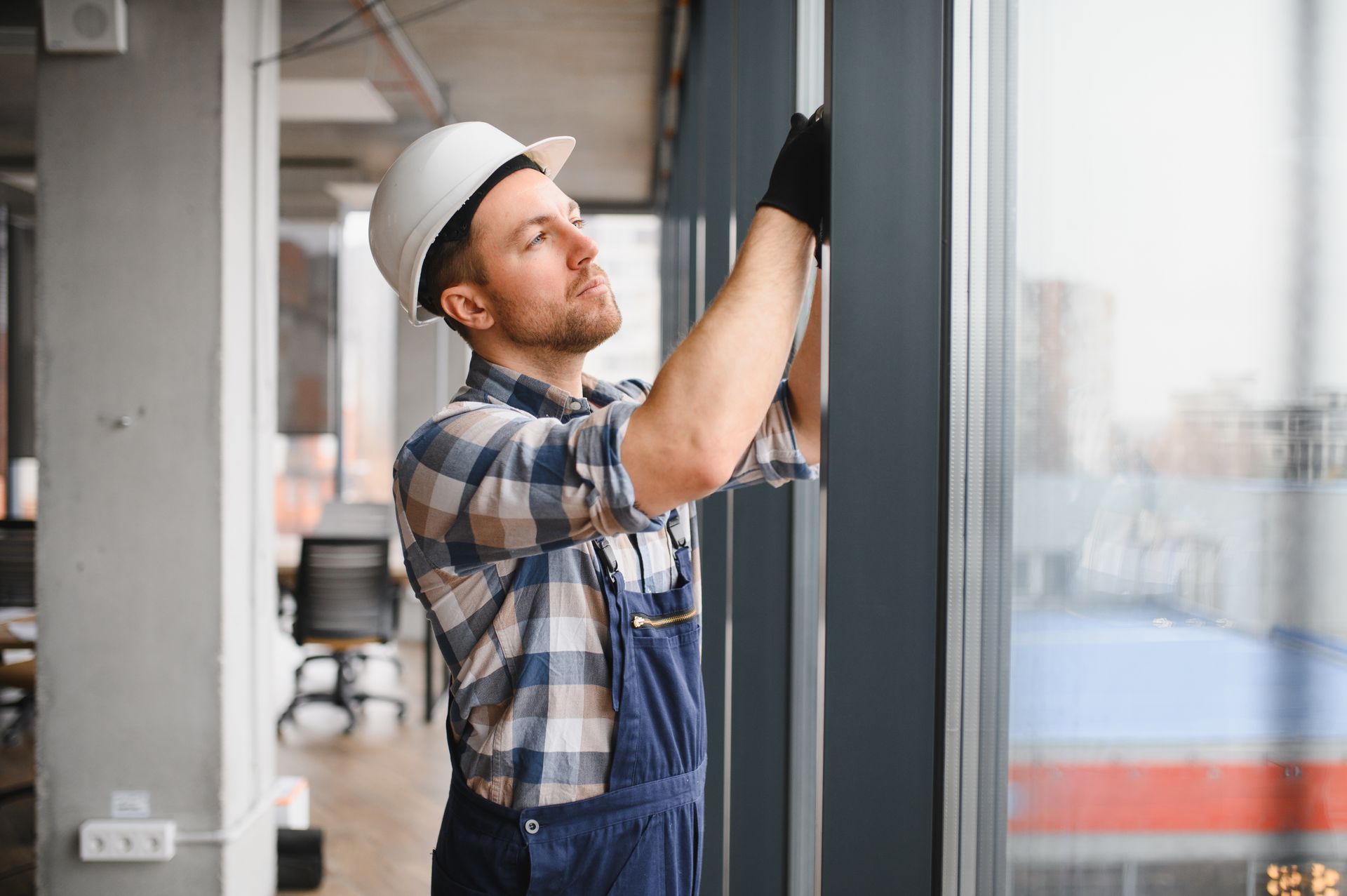 Worker in a hard hat installing a glass panel inside an unfinished building. Worker in a hard hat installing a glass panel inside an unfinished building.
