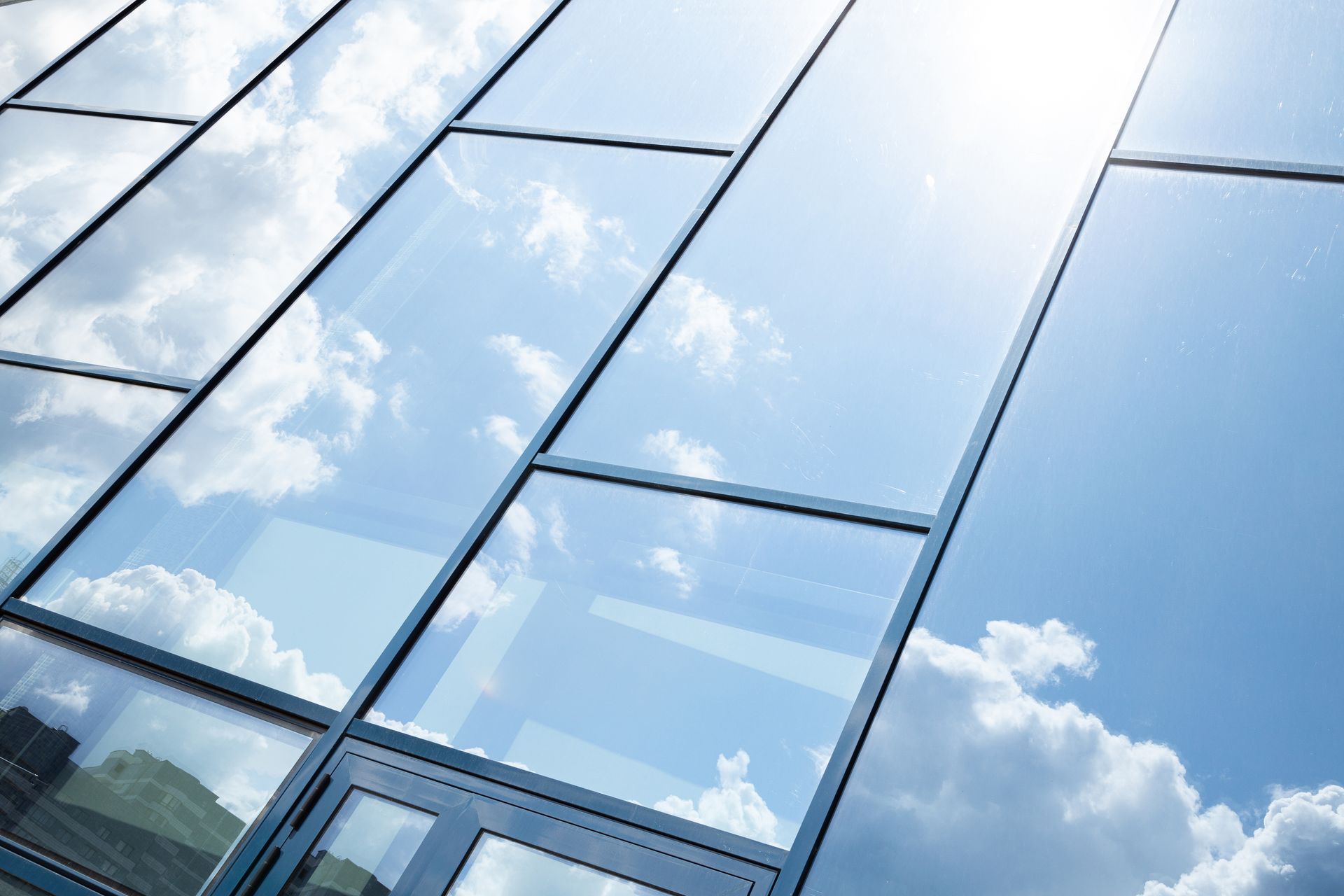 Glass building facade reflecting blue sky and clouds.