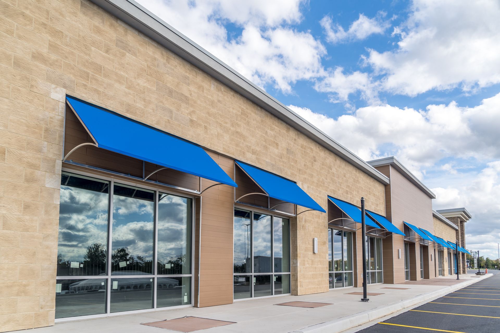 Modern storefront with blue awnings, large windows, and empty sidewalk under cloudy sky.