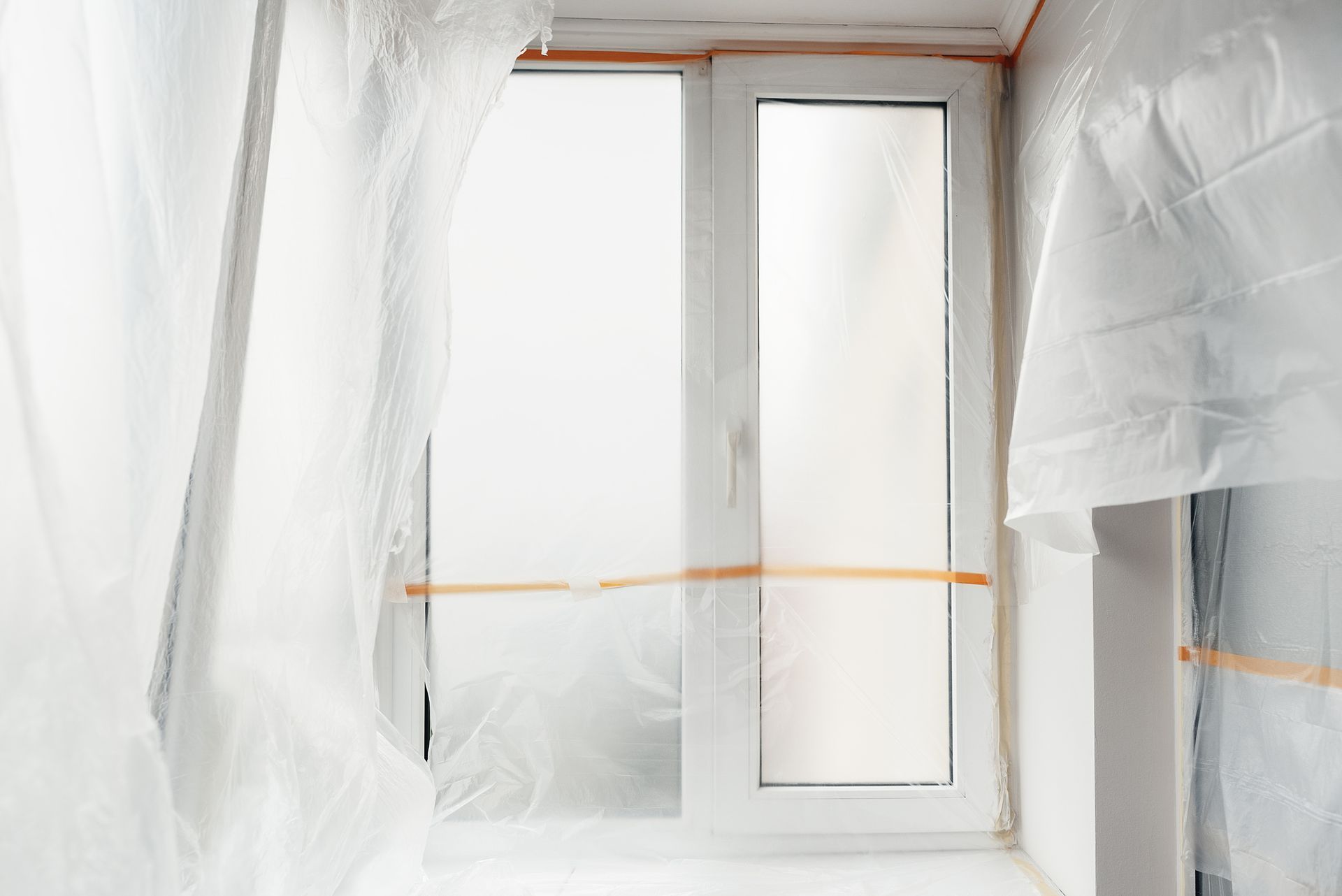 White window covered in plastic sheeting for renovation, taped to the surrounding walls.