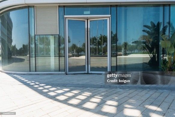 Glass building entrance with double glass doors and reflections of trees and sky on a sunny day