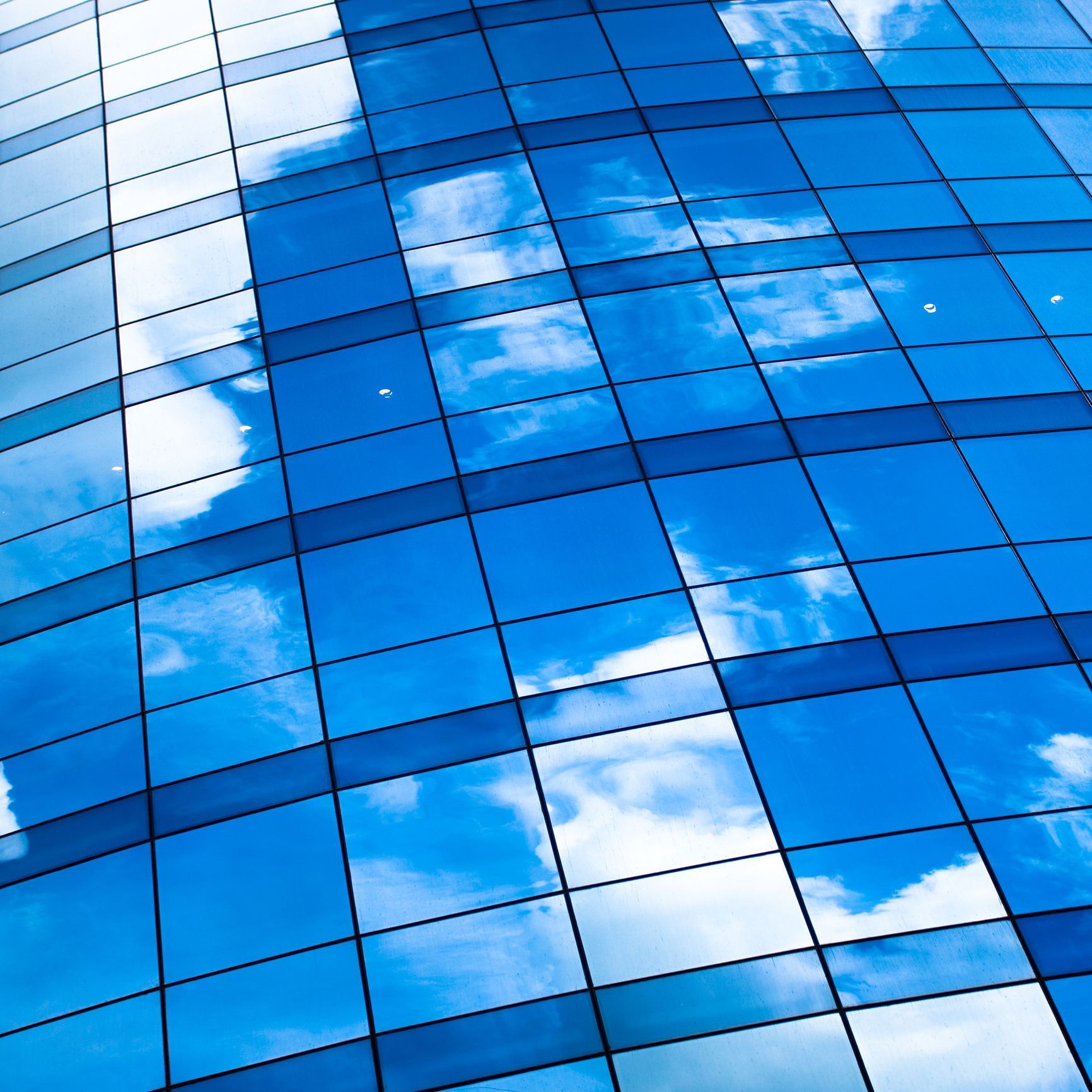 Blue sky and clouds reflected in a glass building's grid-like facade.
