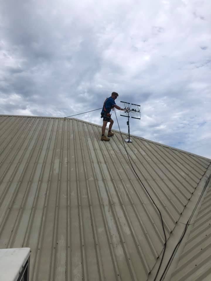 Person on Rooftop Adjusting an Antenna Under a Cloudy Sky — BRC Antenna Service 1 In Banora Point, NSW