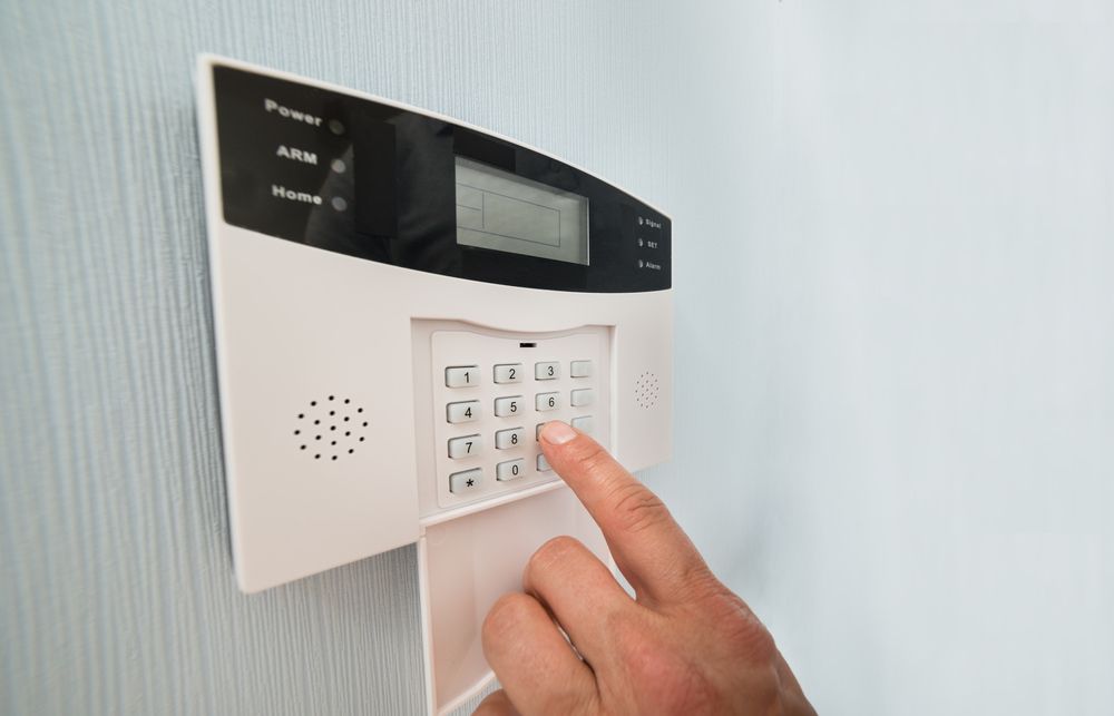Hand entering a security code on a white alarm system keypad mounted on a light blue wall. — BRC Antenna Service 1 In Banora Point, NSW
